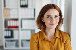 Woman with red hair smiling in front of distant bookcases full of binders