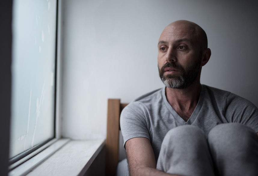 Man with anxiety sitting in wooden chair next to rainy window