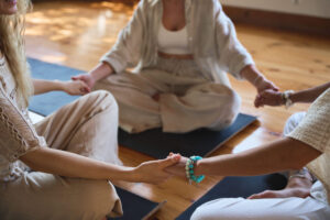 three women holding hands on yoga mats, strengthening support in recovery